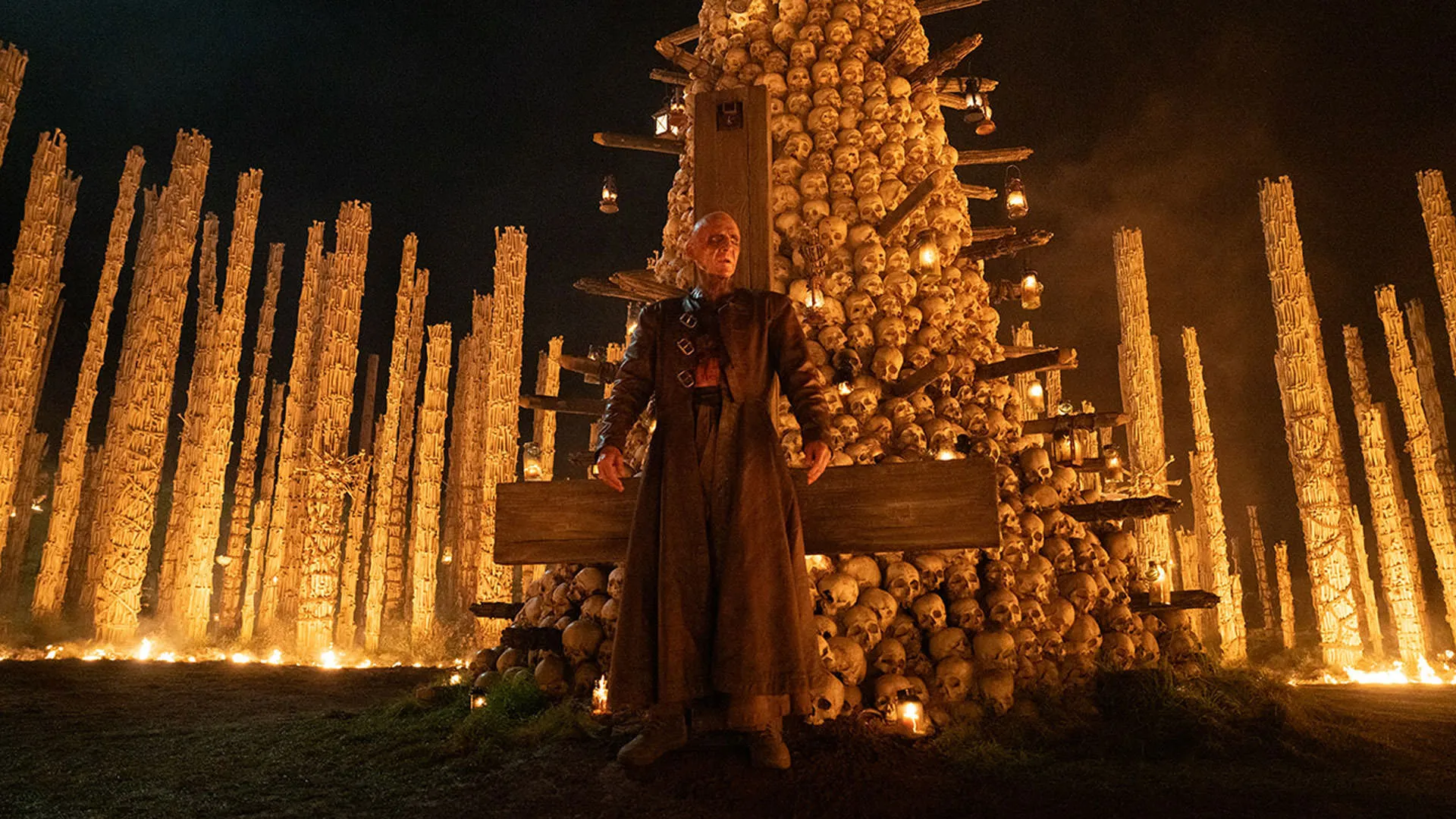 رالف فاینس مقابل یک صلیب وارونه و انبوهی از جمجمه‌ها ایستاده است در نمایی از فیلم ۲۸ سال بعد معبد استخوان نیا داکوستا