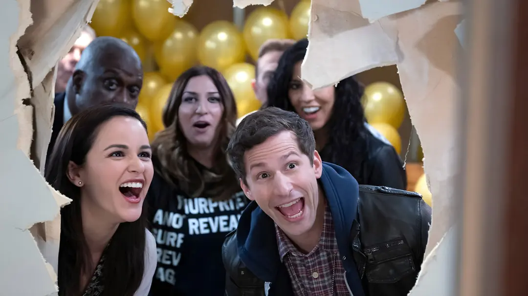 گروهی از بازیگران سریال Brooklyn Nine-Nine از میان یک دیوار گچی نگاه می‌کنند