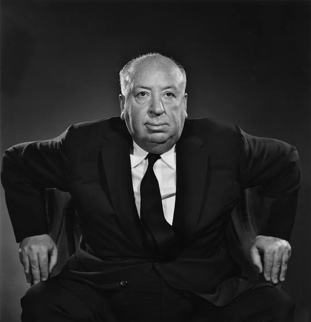 آلفرد هیچکاک (Alfred Hitchcock) با کت و پیراهن سفید در پس‌زمینه تیره