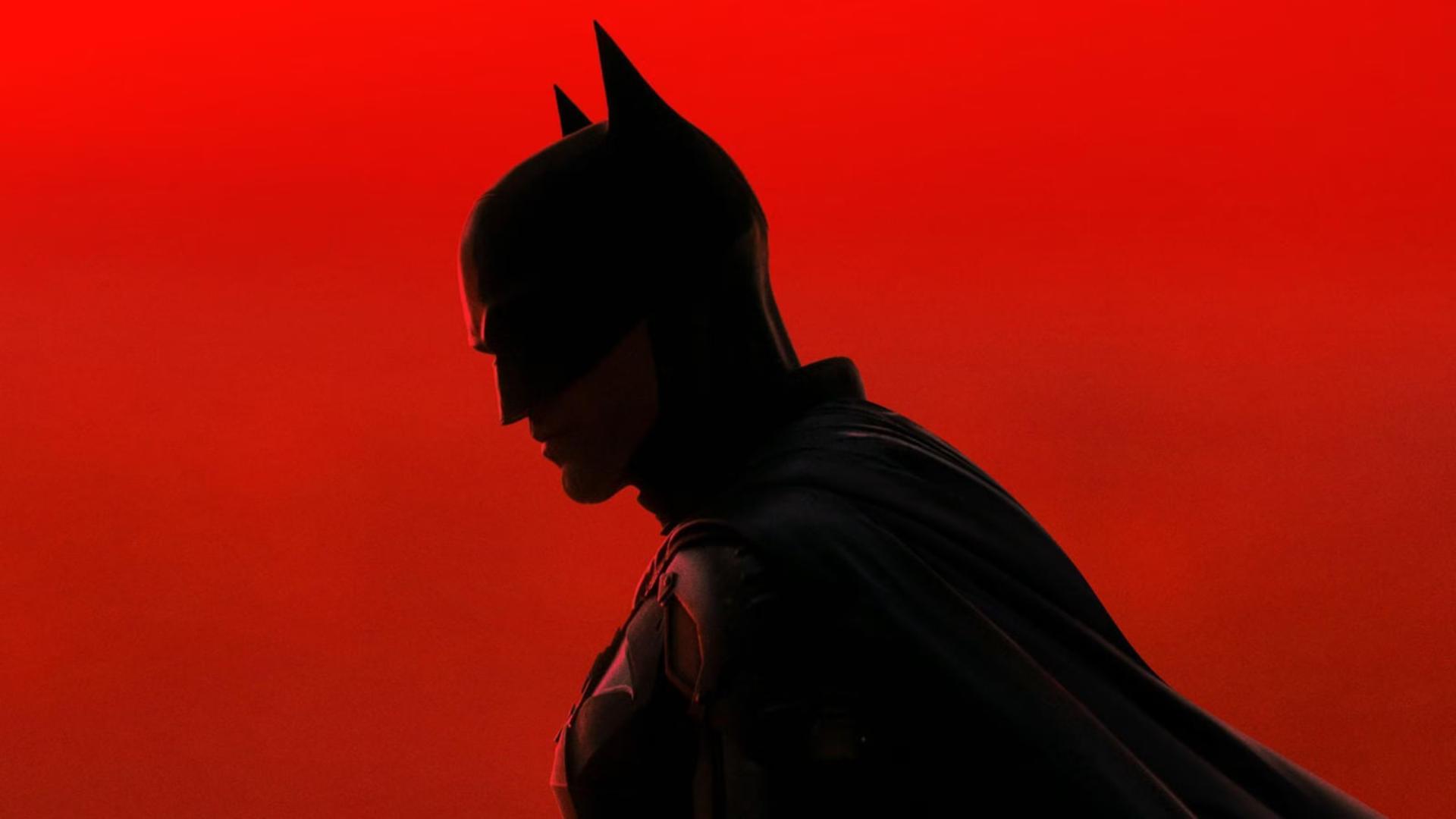 بتمن (Batman) با لباس و ماسک سیاه در پس‌زمینه‌ی قرمز