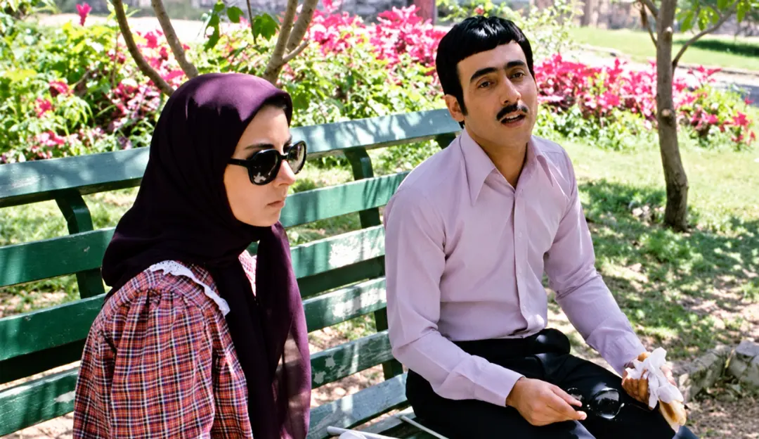 زن با روسری و عینک آفتابی و مرد در کنار هم روی نیمکت پارک