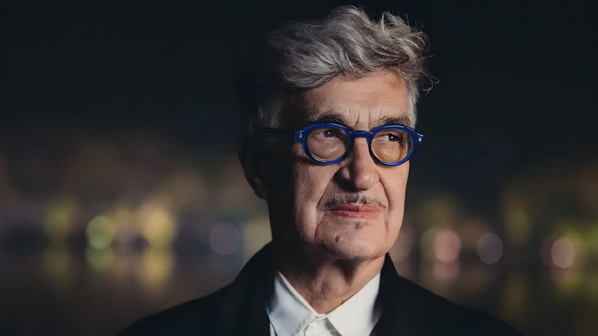 ویم وندرس (Wim Wenders) با عینک با فریم آبی در فضای باز