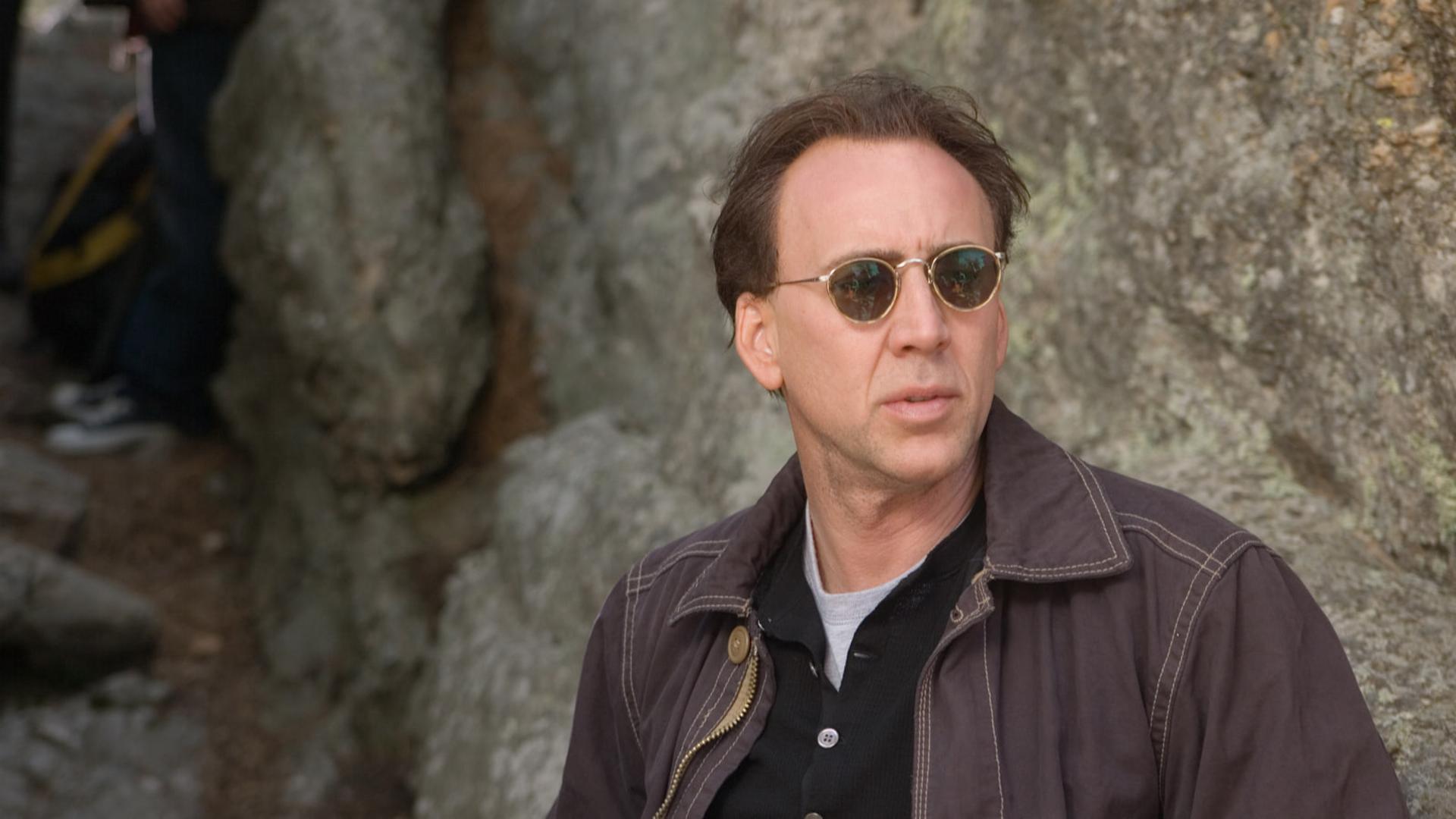 نیکلاس کیج (Nicolas Cage) با عینک آفتابی در محیطی صخره‌ای