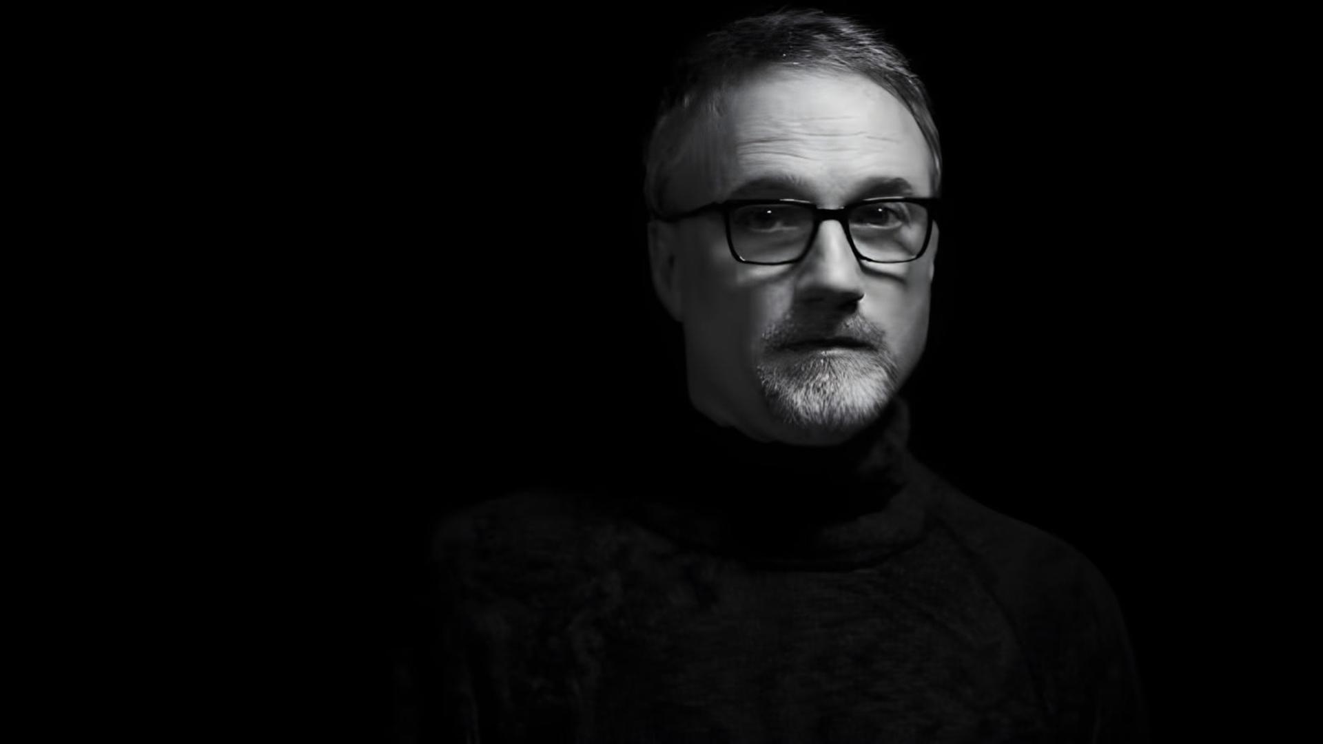 دیوید فینچر (David Fincher) با عینک و لباس تیره در پس‌زمینه سیاه