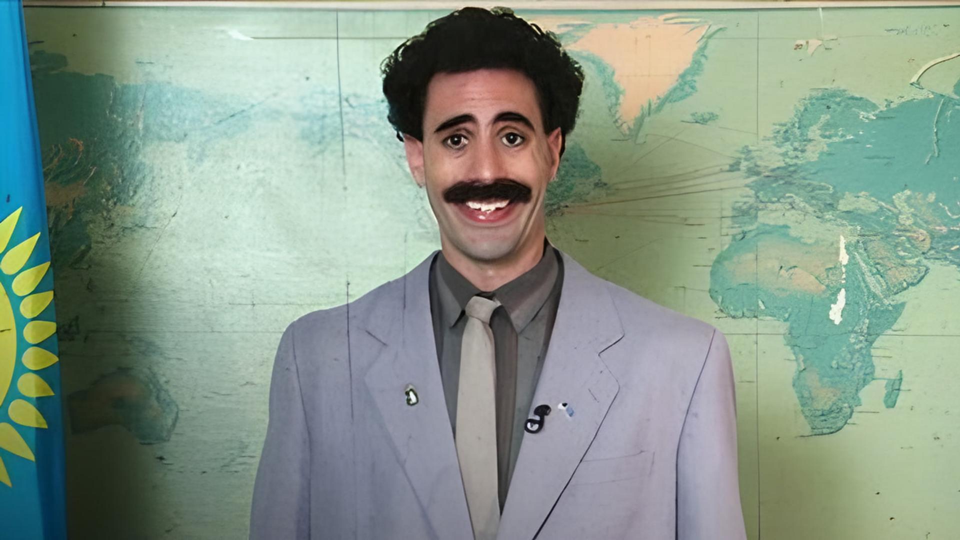ساشا بارون کوهن (Sacha Baron Cohen) با کت روشن مقابل نقشه جهان
