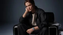 رابرت پتینسون (Robert Pattinson) با لباس تیره روی مبل نشسته است