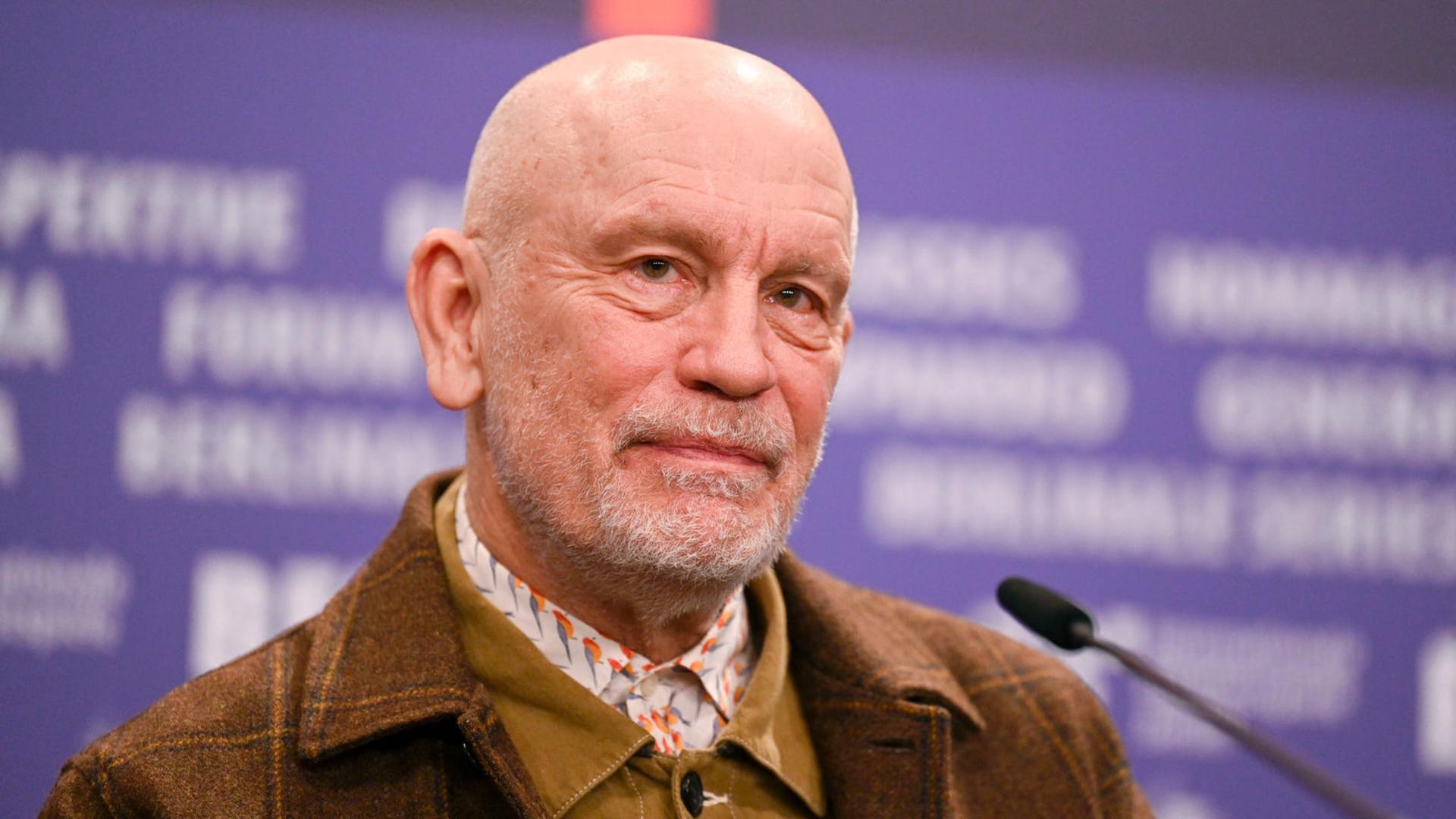 جان مالکوویچ (John Malkovich) در یک نشست خبری با پس‌زمینه بنفش