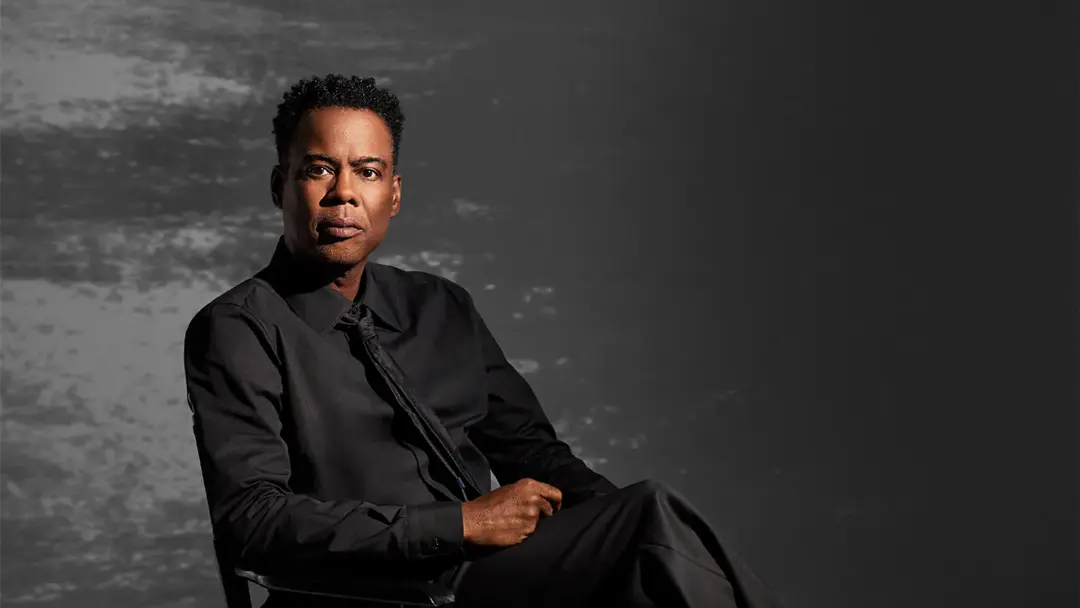 کریس راک (Chris Rock) با لباس رسمی مشکی در مقابل پس‌زمینه خاکستری