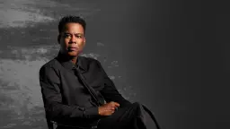 کریس راک (Chris Rock) با لباس رسمی مشکی در مقابل پس‌زمینه خاکستری