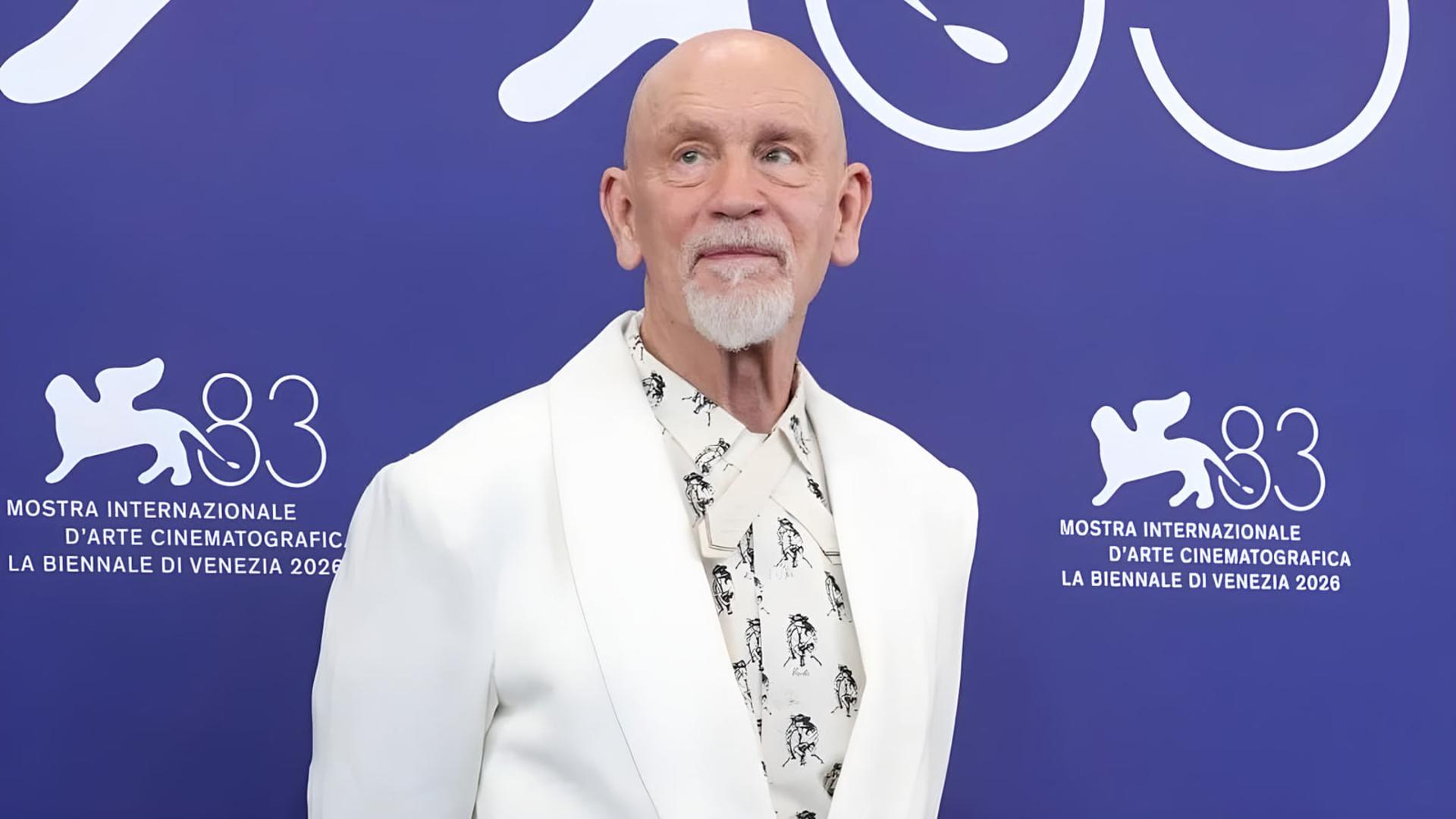 جان مالکوویچ (John Malkovich) با کت سفید در مقابل پس‌زمینه آبی جشنواره