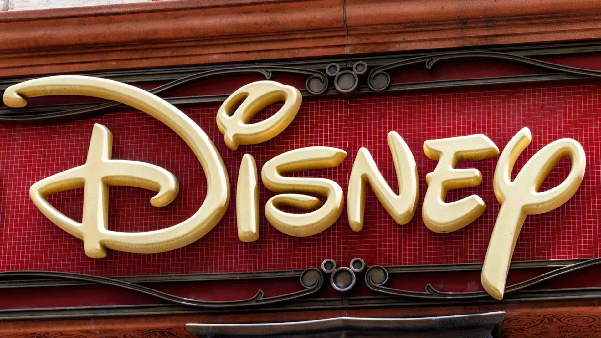 لوگوی طلایی شرکت دیزنی (Disney) روی پس‌زمینه‌ای قرمز با طرح‌های تزئینی