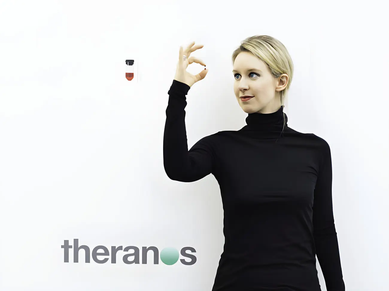 الیزابت هومز (Elizabeth Holmes) در کنار لوگوی شرکت ثرانووس (Theranos)