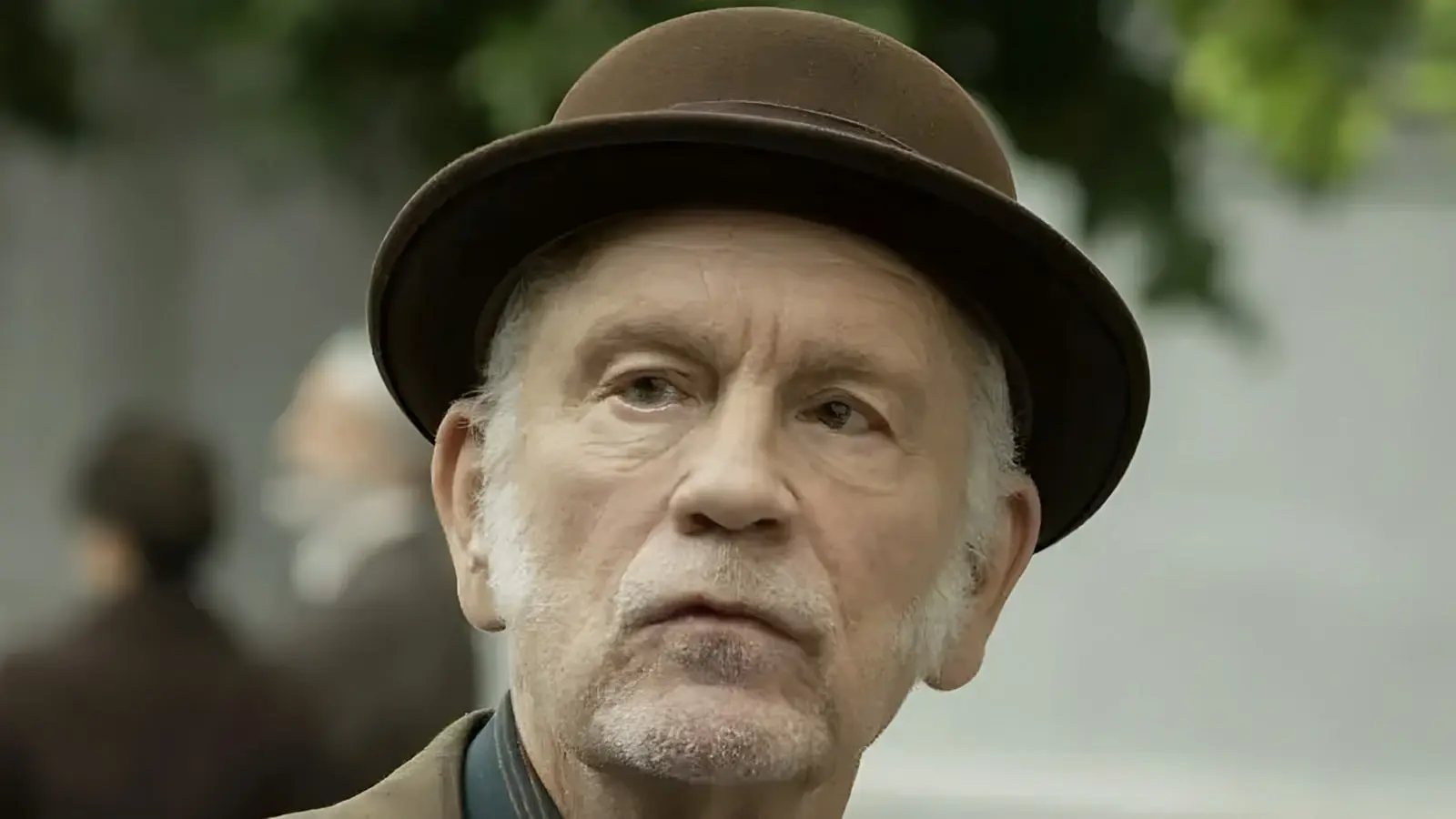 چهره نزدیک جان مالکوویچ (John Malkovich) با کلاه قهوه‌ای کلاسیک