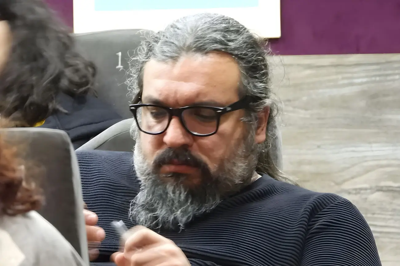 مردی با عینک و ریش خاکستری در یک نشست یا رویداد