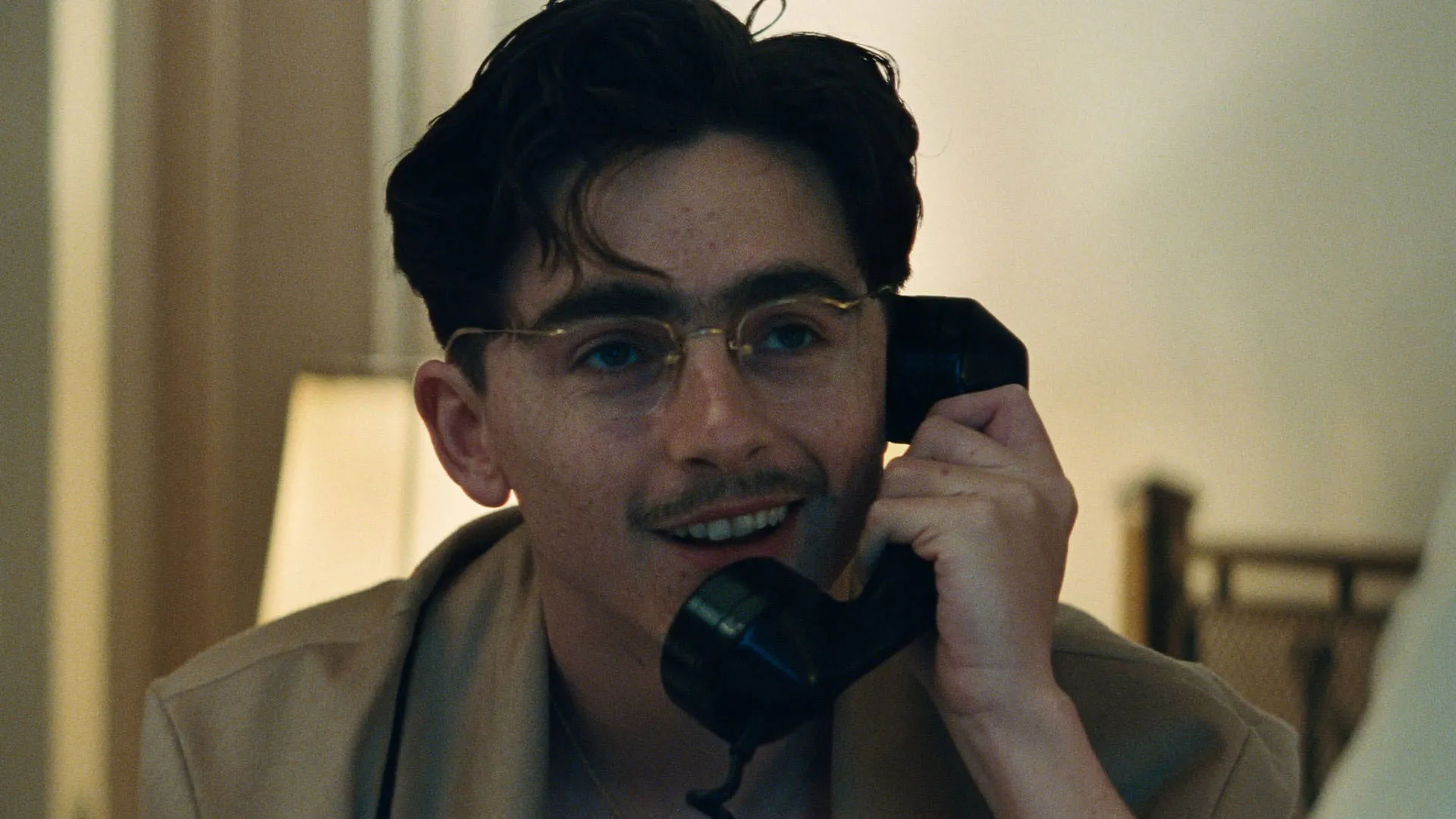 تیموتی شالامی با تلفن حرف می‌زند و لبخند به لب دارد در نمایی از فیلم مارتی معظم جاش سفدی