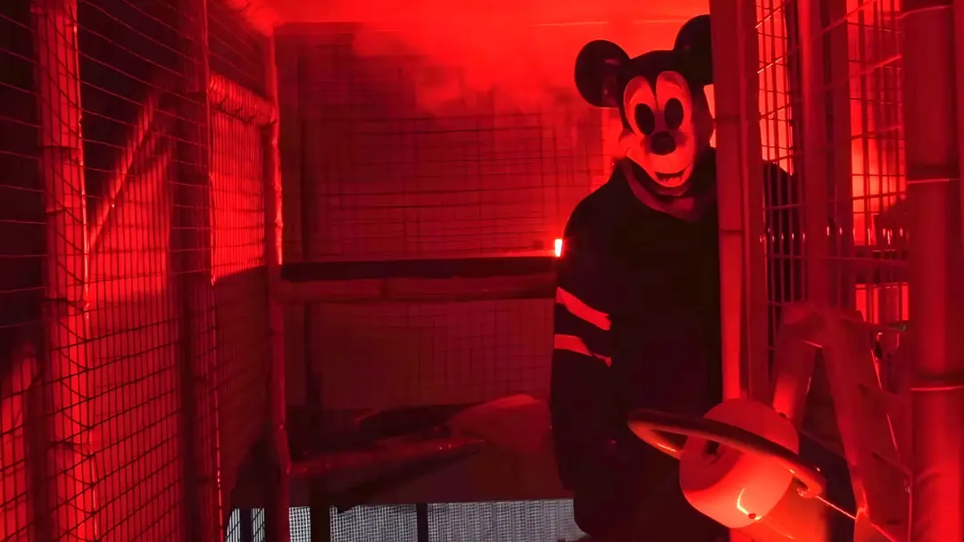 میکی‌ماوس (Mickey Mouse) در محیطی تاریک با نورپردازی قرمز و حصارهای فلزی
