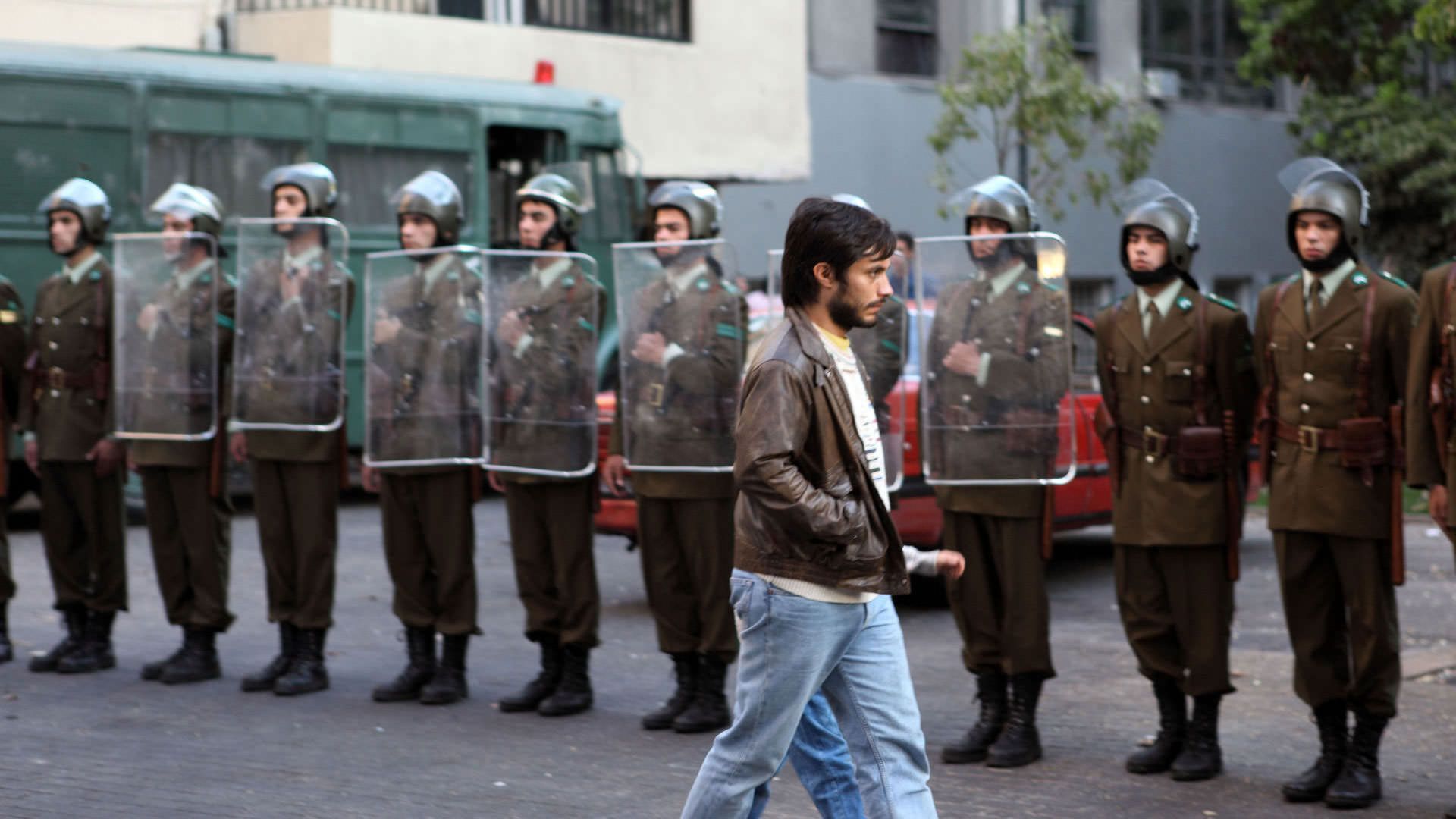 گائل گارسیا برنال از جلوی سربازانی که سپر به دست دارند میگذرد در نمایی از فیلم نه به کارگردانی پابلو لارائین