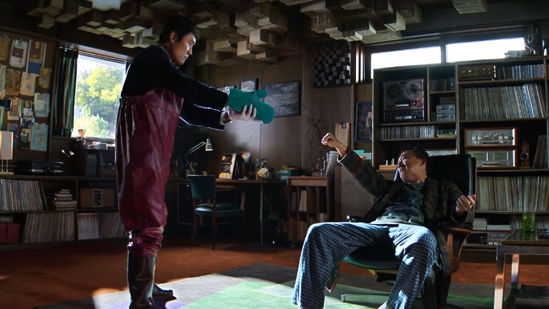 لیو بیونگ هون با لباس باغبانی ایستاده است مقابل لی سونگ مین که وسط اتاقی پر از صفحات موسیقی نشسته است در نمایی از فیلم چاره‌ای نیست به کارگردانی پارک چان ووک