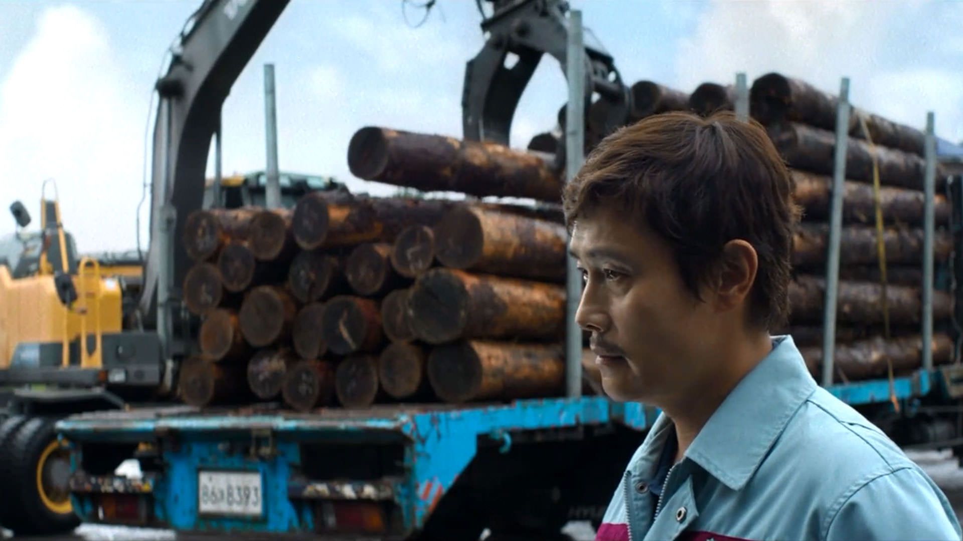 لی بیونگ هون مقابل کامیونی که بار الوار دارد ایستاده است در نمایی از فیلم چاره‌ای نیست به کارگردانی پارک چان ووک