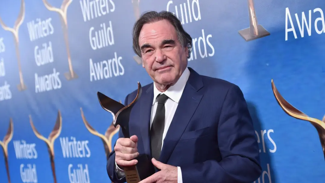 اولیور استون (Oliver Stone) در حال holding کردن تندیس جوایز نویسندگان