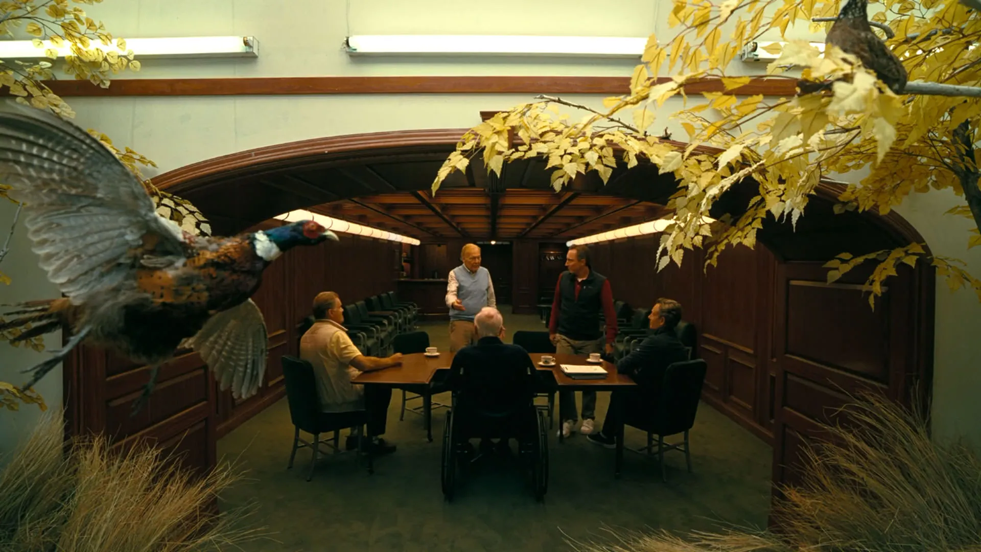 مردانی جلسه برگزار کرده‌اند در حالی که درخت و پرنده در پیش زمینه‌ی نما دیده می‌شوند در نمایی از فیلم نبرد پشت نبرد پل توماس اندرسون