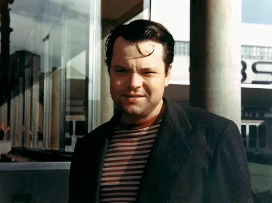 اورسن ولز (Orson Welles) با کت تیره و تی‌شرت راه راه در فضای باز