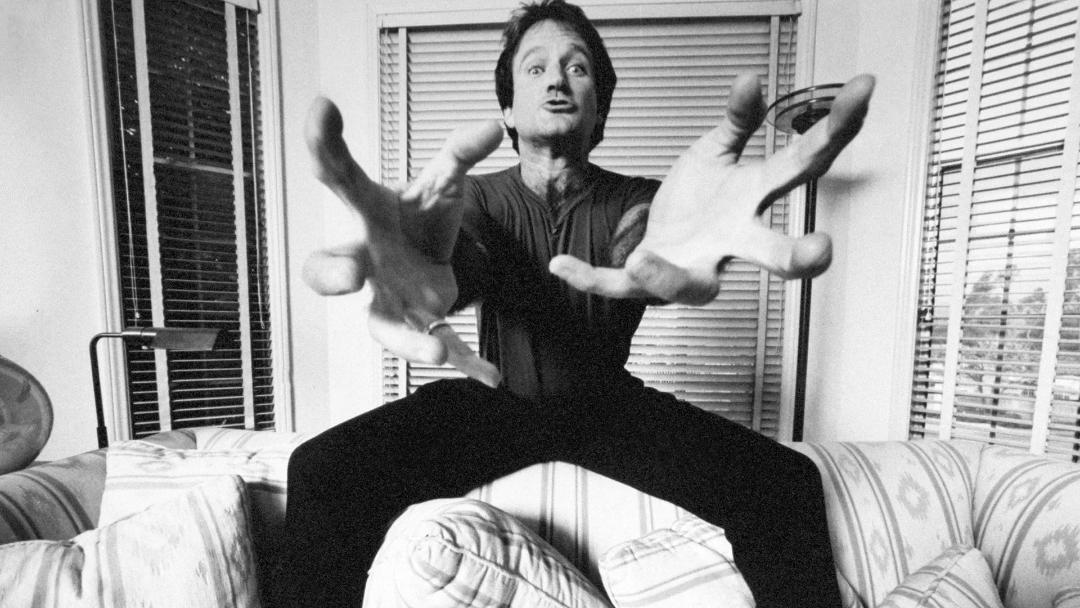 رابین ویلیامز (Robin Williams) با دست‌های باز در فضای داخلی خانه