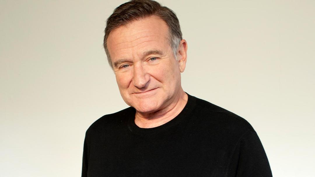 رابین ویلیامز (Robin Williams) با لبخندی ملایم در مقابل پس‌زمینه روشن