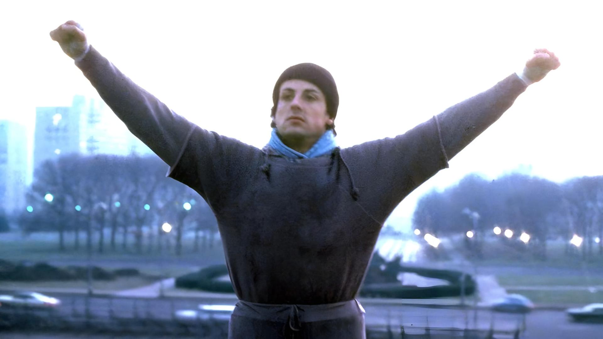 راکی بالبوا (Rocky Balboa) با دست‌های باز در بالای پله‌ها ایستاده است