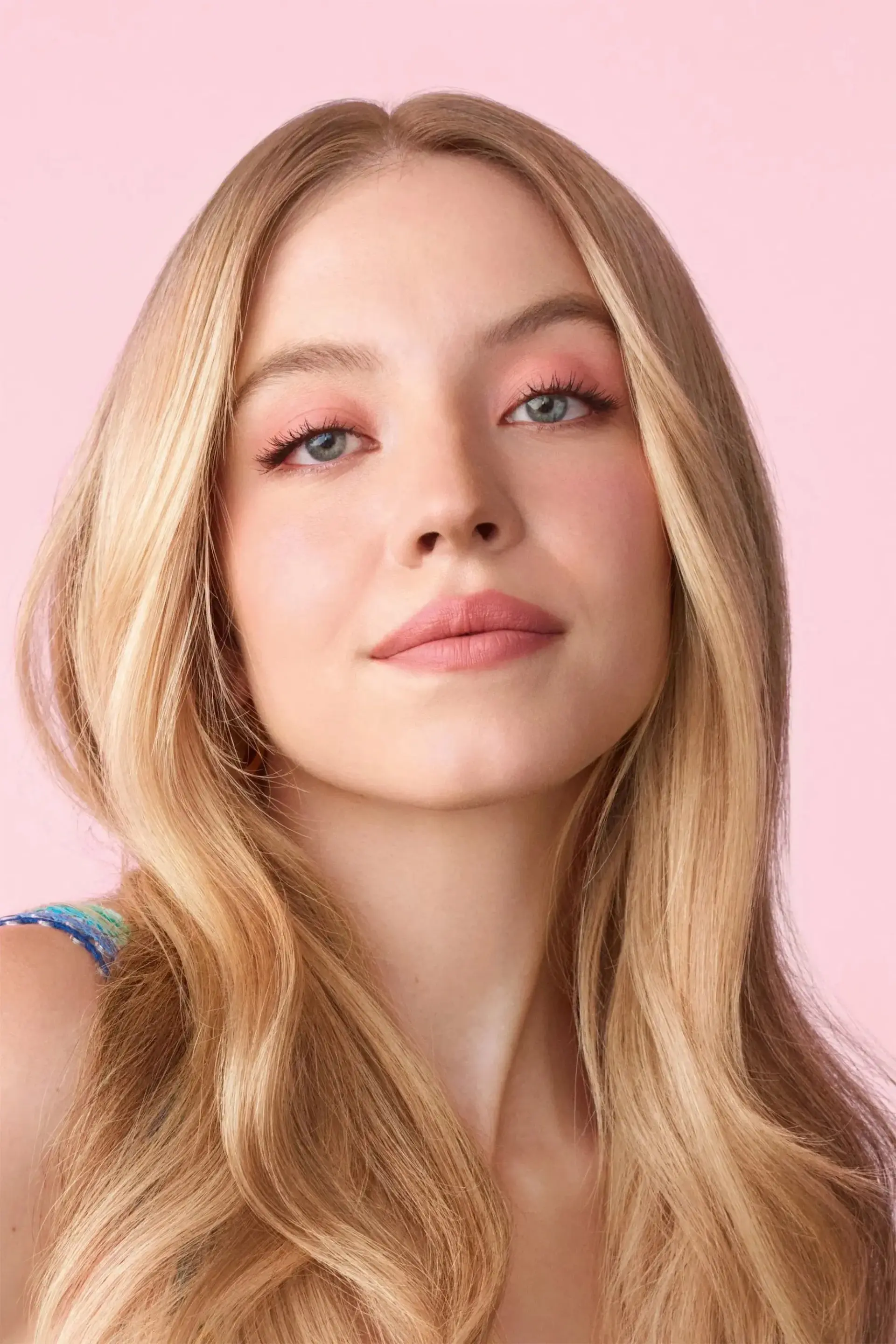 سیدنی سوئینی (Sydney Sweeney) با موهای بلوند در مقابل پس‌زمینه صورتی
