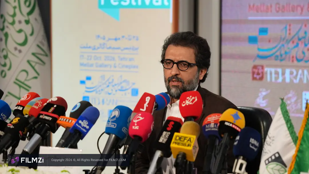 مردی با عینک در میان میکروفون‌های خبرنگاران در نشست خبری جشنواره فیلم تهران