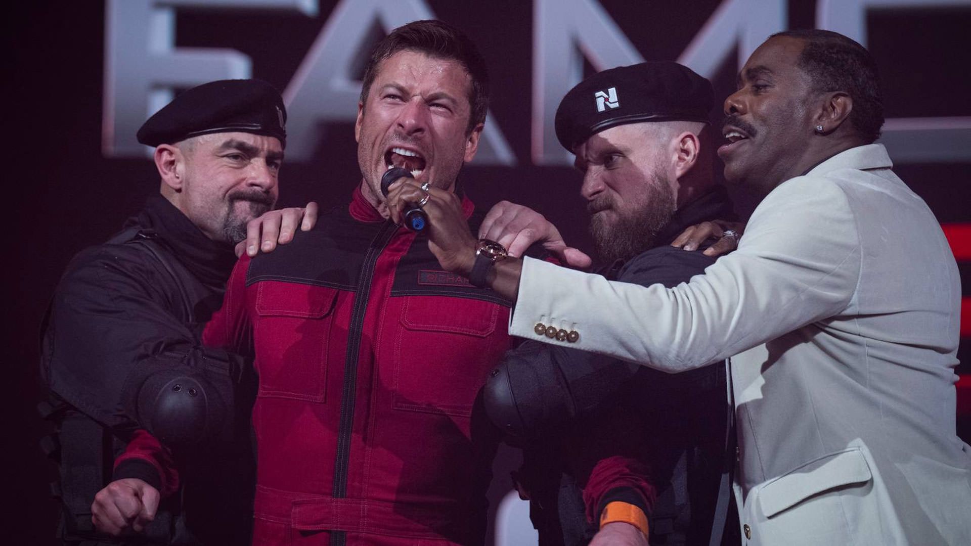 کولمن دومینگو در کنار دو سربازی ایستاده است که گلن پاول را که یونیفرم قرمز بر تن دارد دستگیر کرده اند و جلوی او میکروفون میگیرد در نمایی از فیلم مرد فراری ادگار رایت