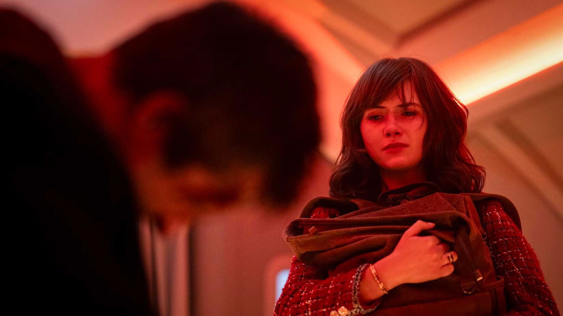 امیلیا جونز در هواپیمایی با نورپردازی قرمز کوله‌ای را در آغوش گرفته است در نمایی از فیلم مرد فراری ادگار رایت