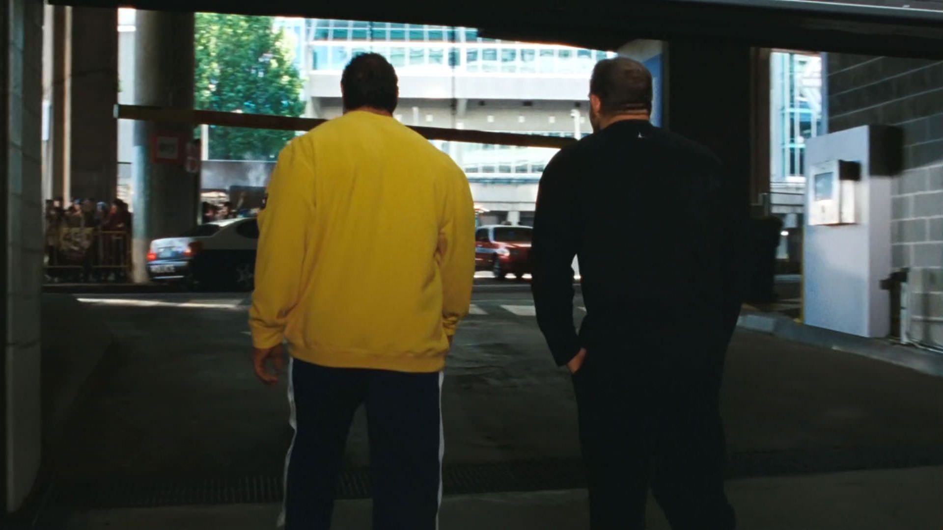 دواین جانسون راک با لباس زرد پشت به دوربین کنار رایان بادر راه می‌رود در نمایی از فیلم ماشین کوبنده به کارگردانی بنی سفدی