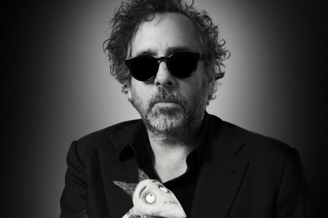 تیم برتون (Tim Burton) با عینک آفتابی سیاه در مقابل پس‌زمینه تیره