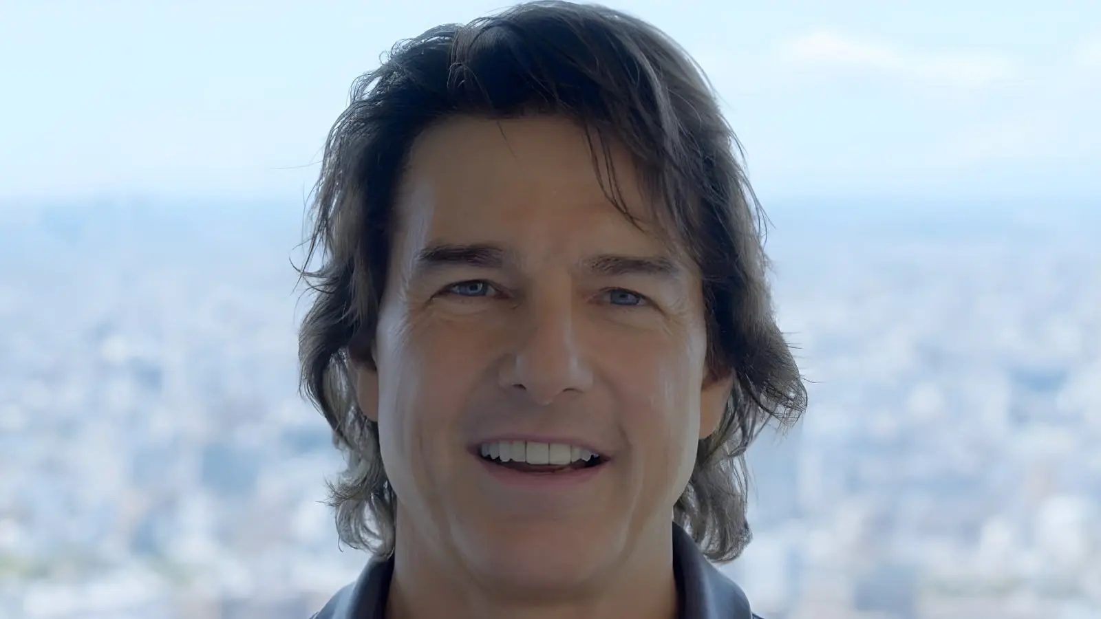 تام کروز (Tom Cruise) با چهره‌ای خندان در مقابل پس‌زمینه‌ای از نمای شهر