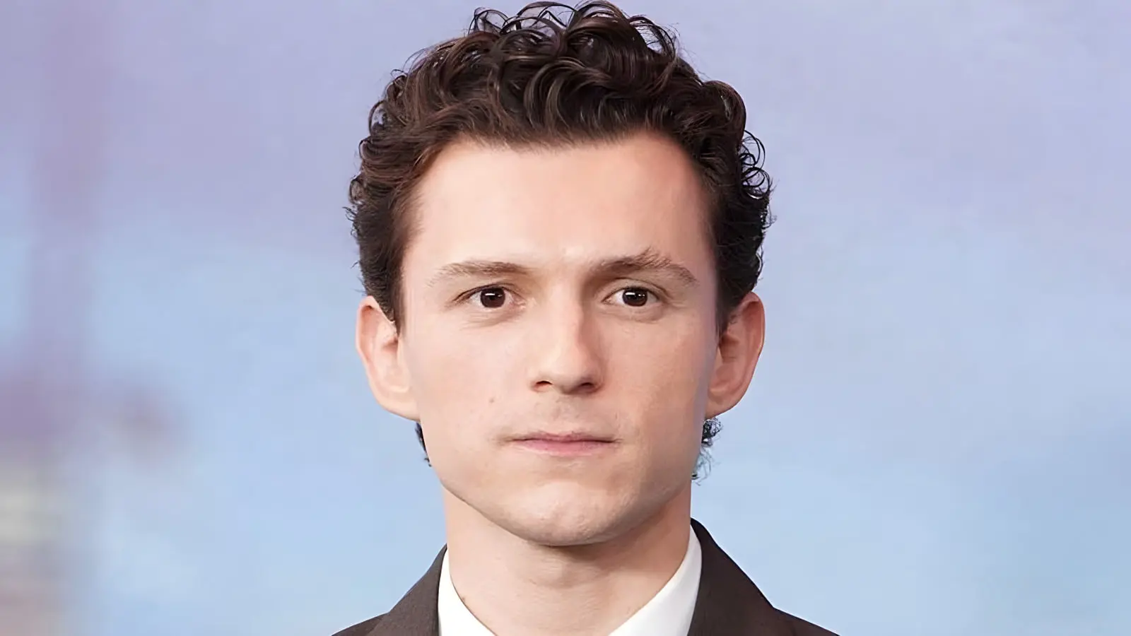 چهره نزدیک تام هالند (Tom Holland) با موهای فر و نگاه مستقیم