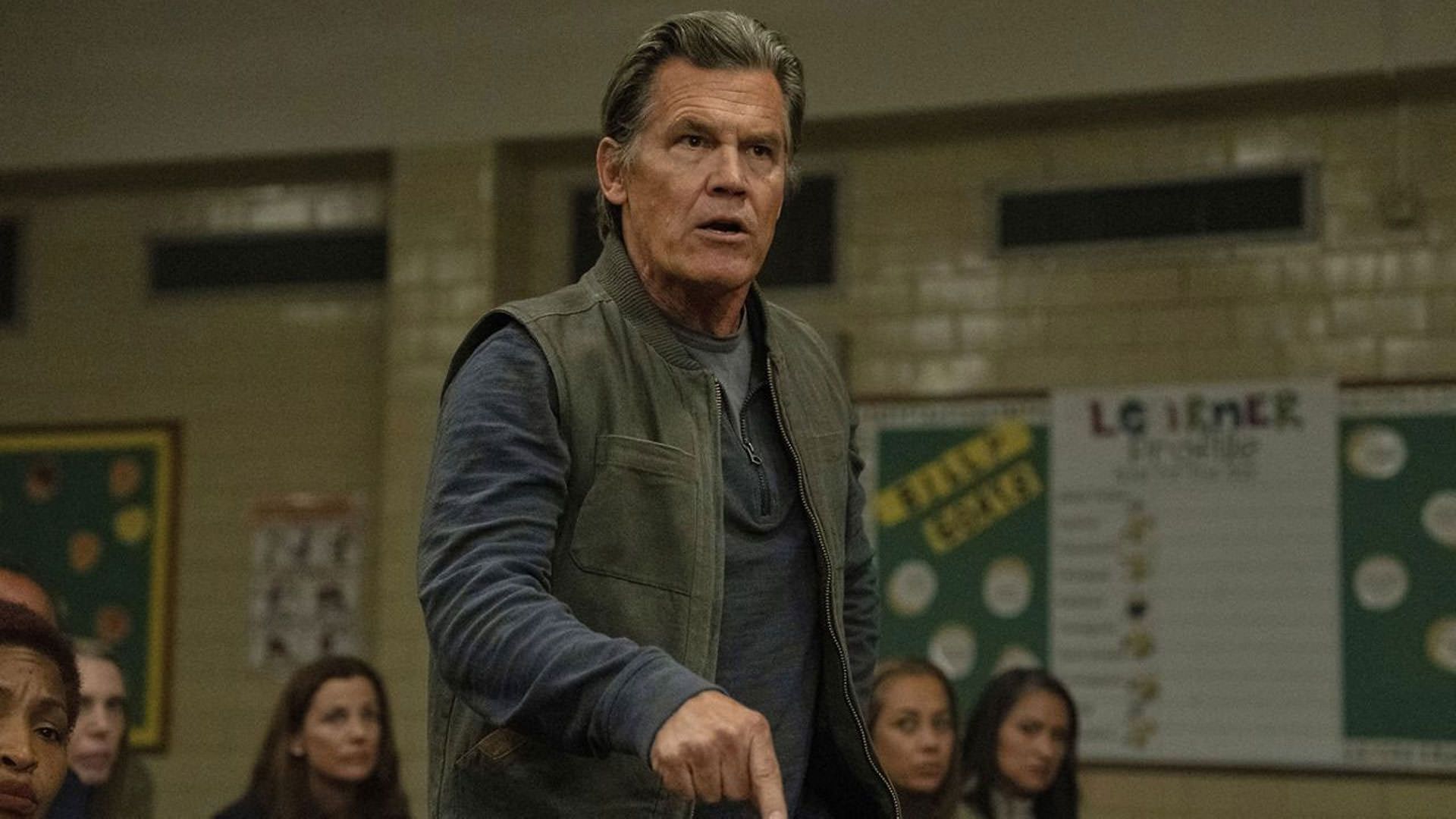 جاش برولین در میان جمعیتی نشسته از جایش برخواسته است و با عصبانیت فریاد میزند در نمایی از فیلم سلاح ها به کارگردانی زک کرگر