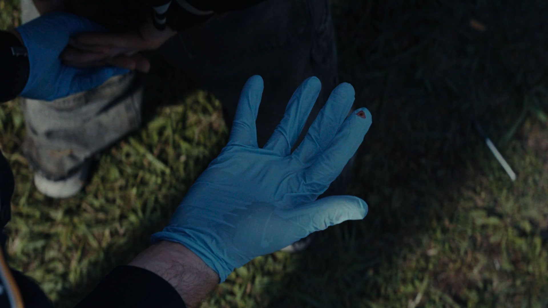 دست زخمی پلیسی که دستکشی آبی بر دست دارد در نمایی از فیلم سلاح ها به کارگردانی زک کرگر