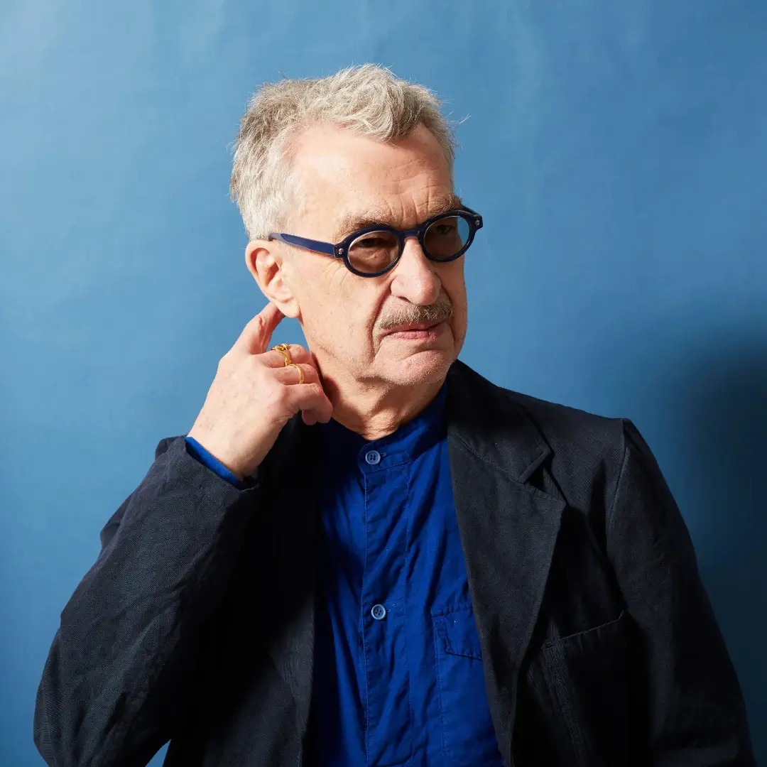 ویم وندرس (Wim Wenders) با عینک تیره در مقابل پس‌زمینه آبی