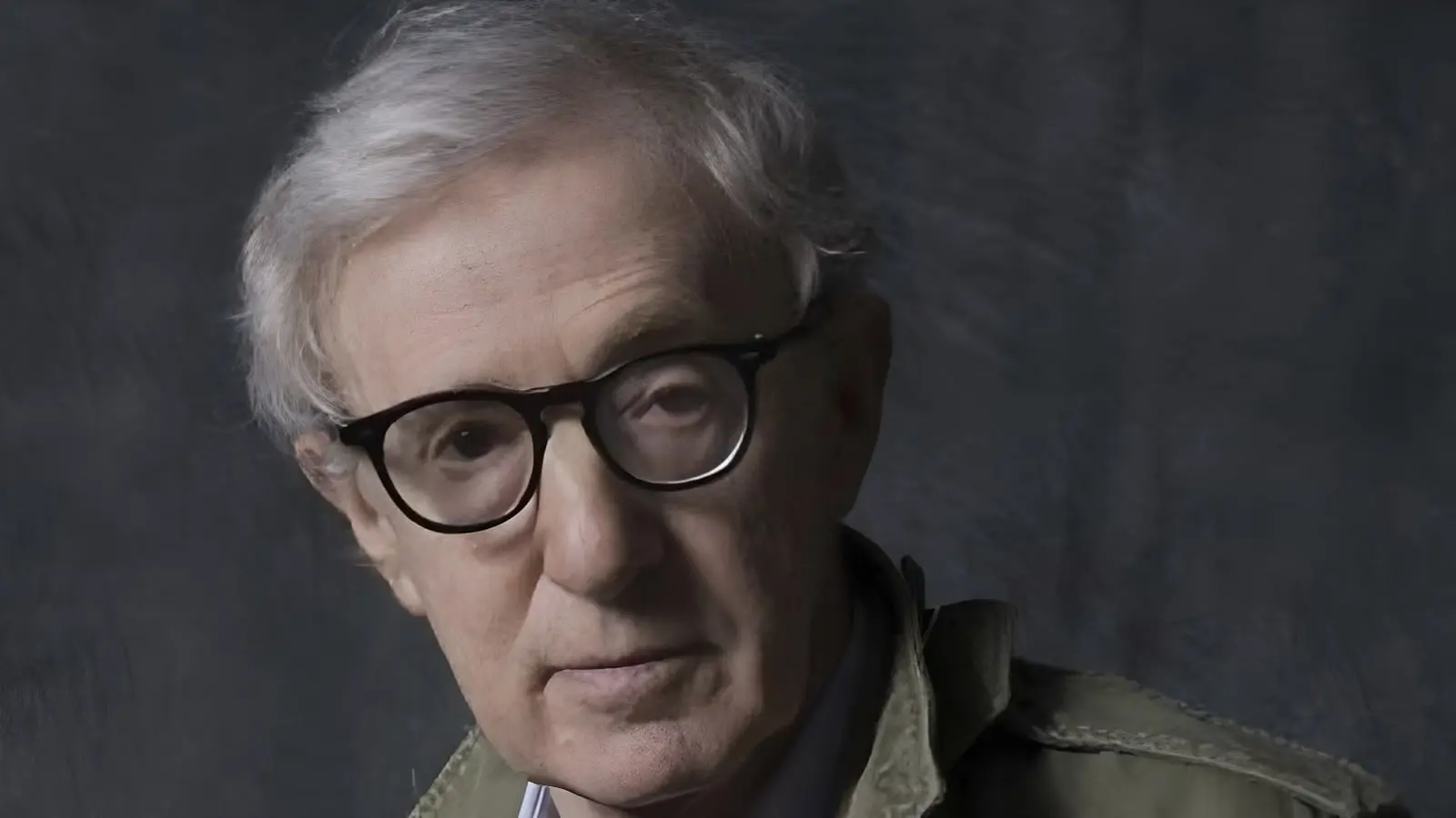 وودی آلن (Woody Allen) با عینک مشکی در مقابل پس‌زمینه تیره